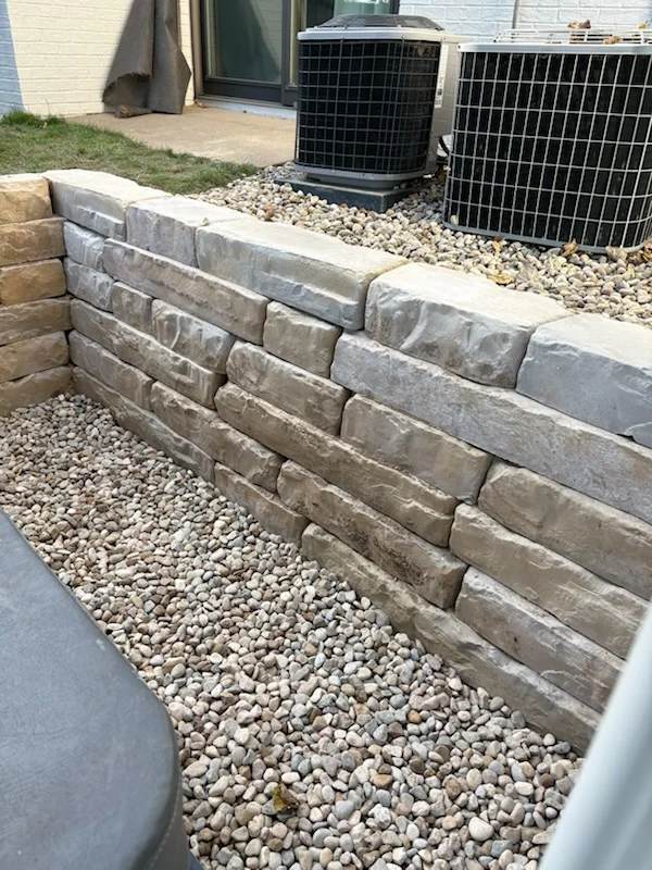 Stacked concrete retaining wall with gravel base and drainage rock