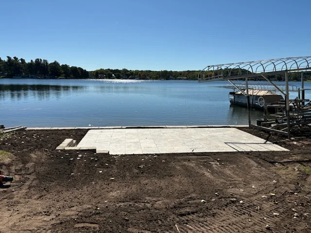 Concrete pad installation on waterfront beach with boat dock structure visible