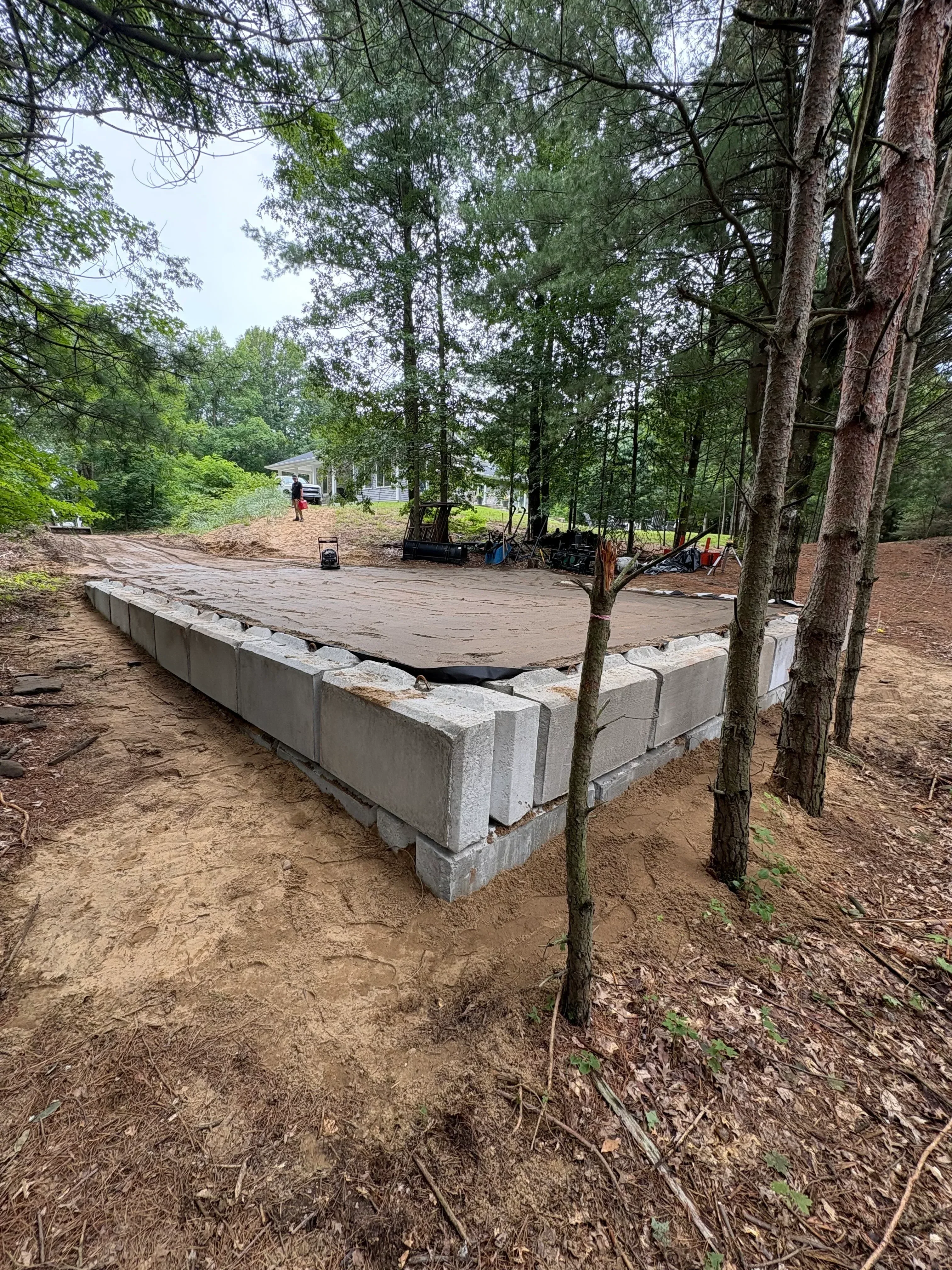 Concrete block retaining wall installation on sloped terrain with proper drainage and backfill