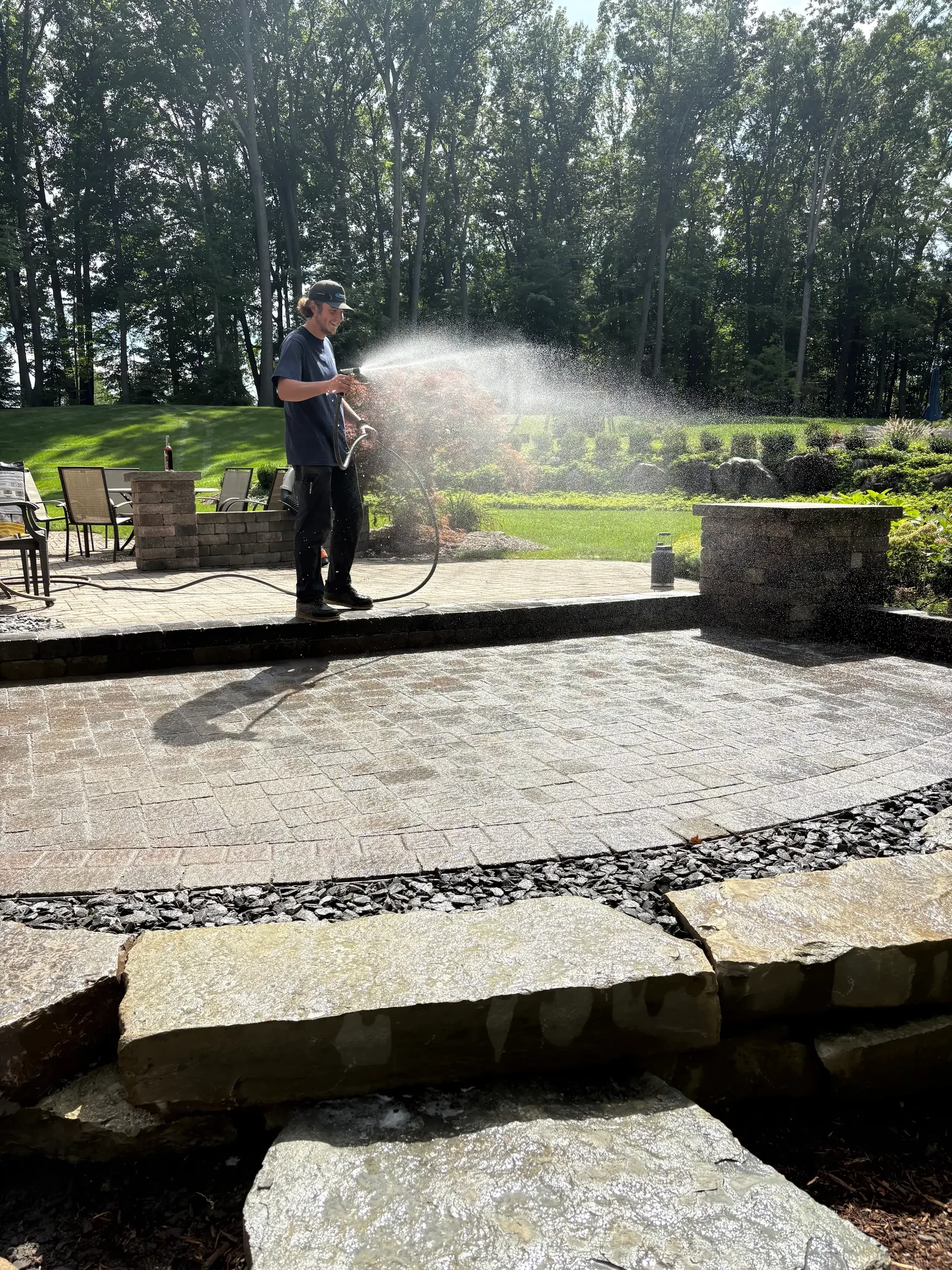 Pressure washing stone paver patio with black rock edging and brick planter wall
