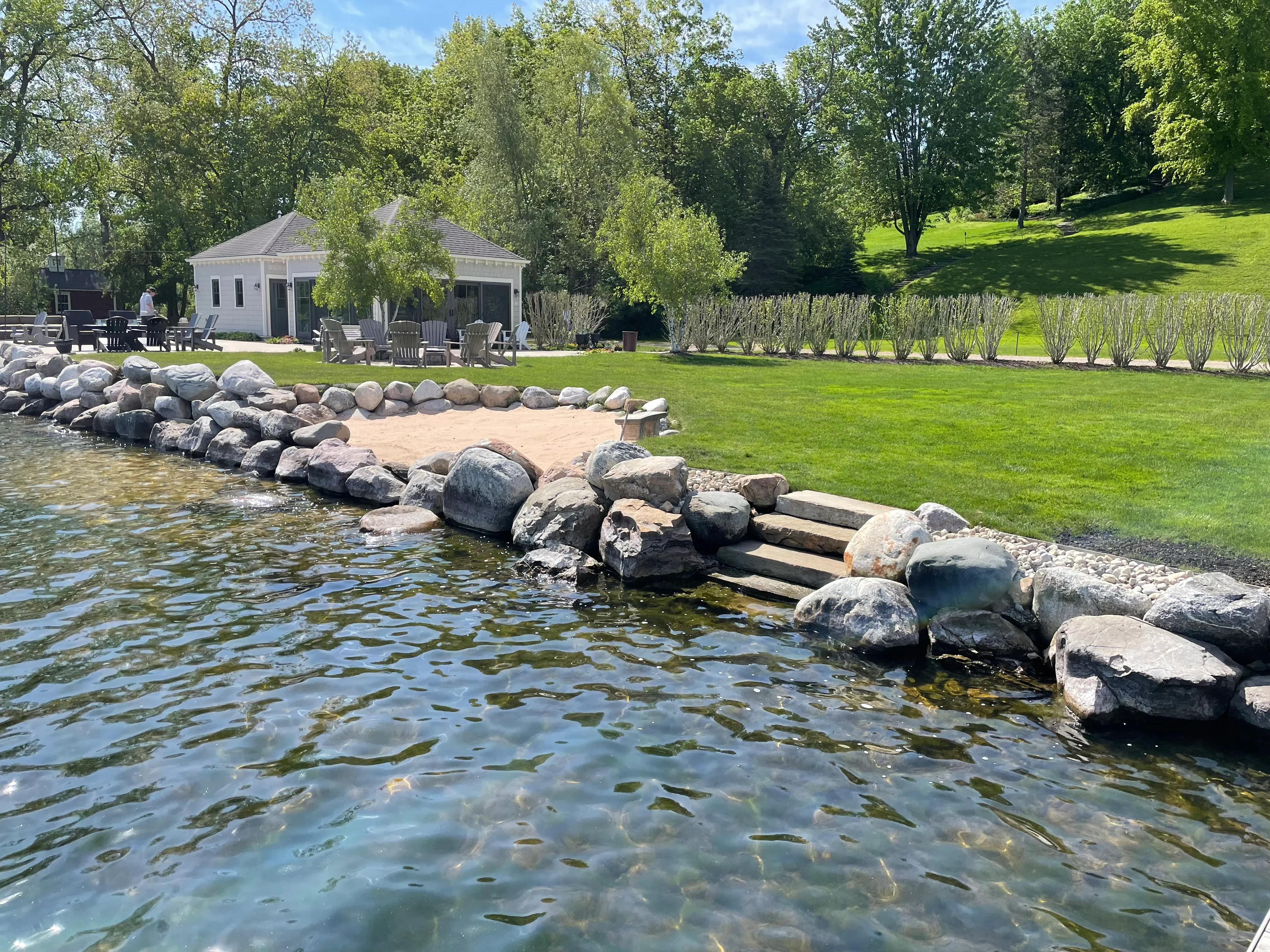 Boulder shoreline with timber steps, sandy beach, and manicured lawn along waterfront property