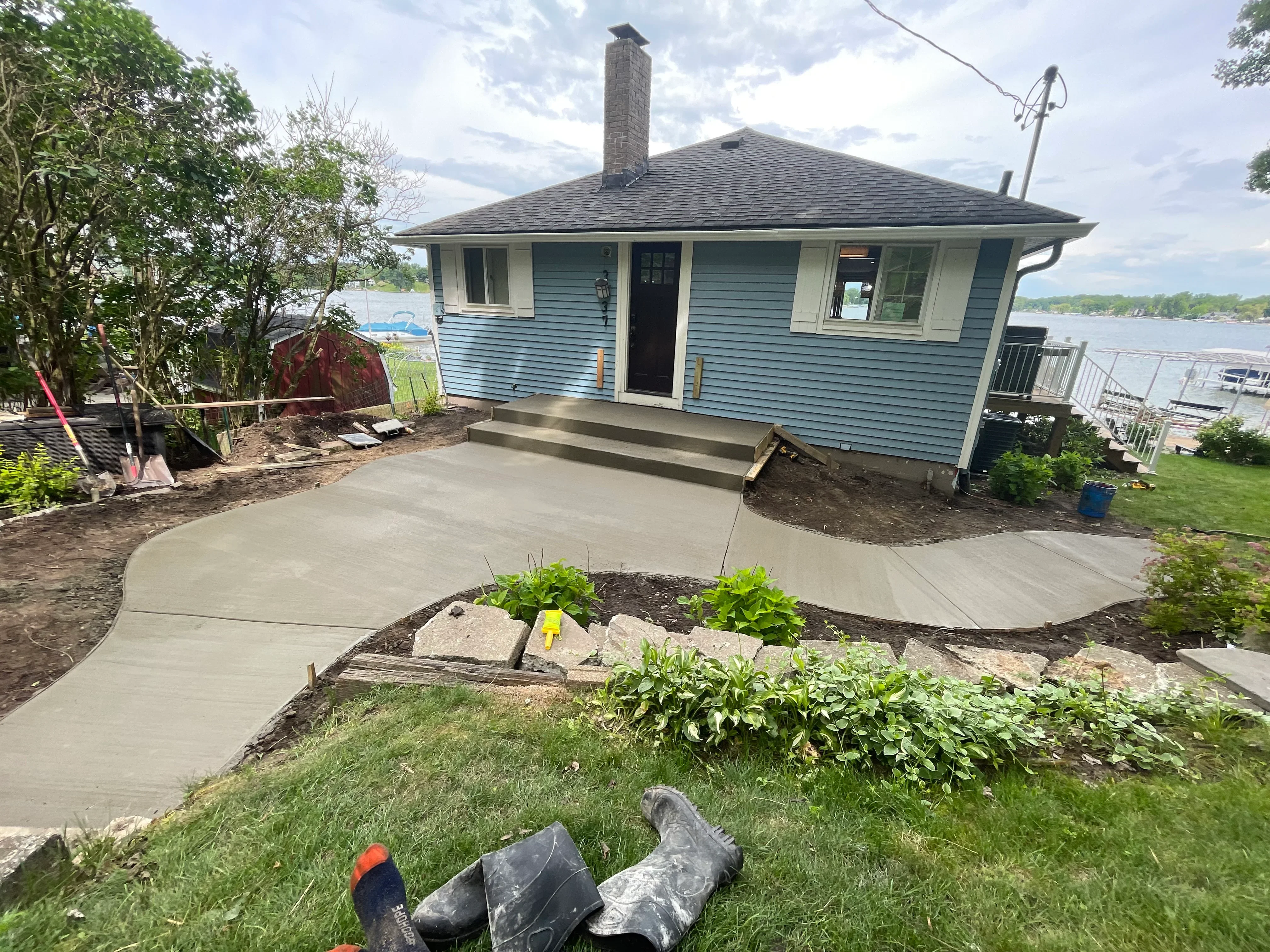 Newly poured concrete patio with curved design, stone-edged landscape beds, and concrete steps at waterfront home
