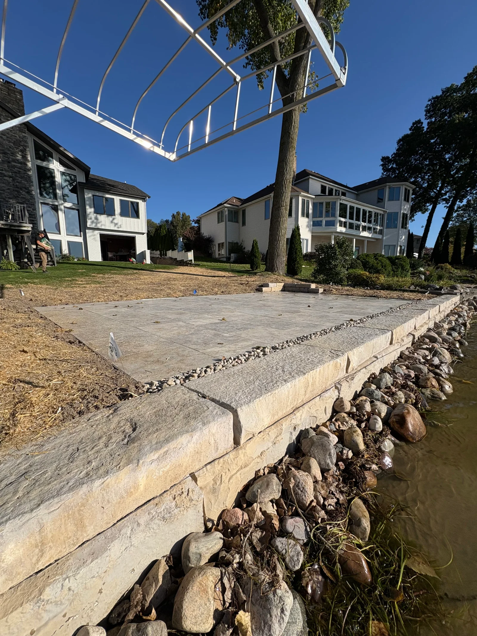 Gray paver patio with cut-stone retaining wall and rock armoring along waterfront